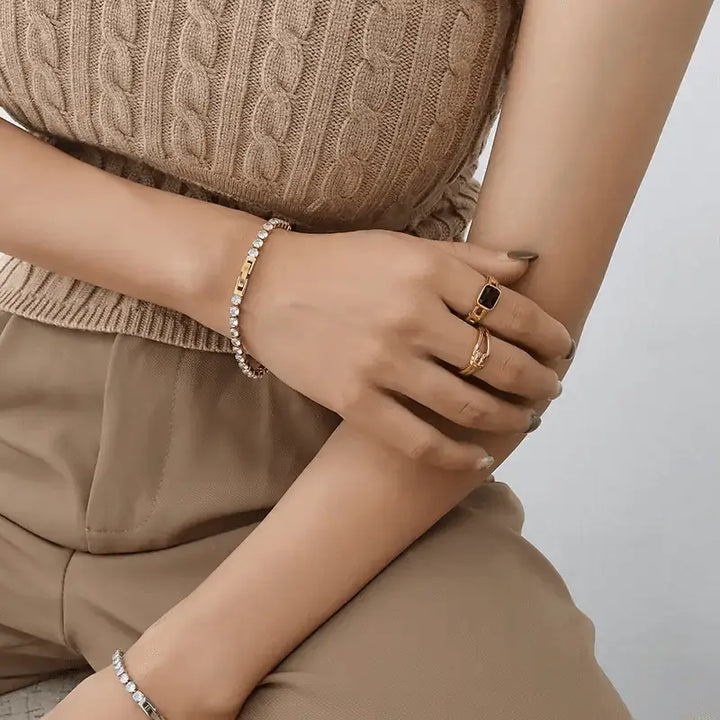 Gold and silver jewelry including a stunning Zircon Bracelet on hands against beige knitwear